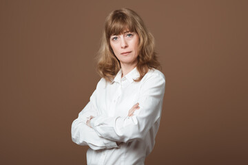 Attractive Middle-Aged Businesswoman. Portrait of Confident Lady with Blonde Hair in a White Shirt, Standing in an Assertive Pose with Crossed Arms. Concept of a Professionalism, Confidence, and Poise