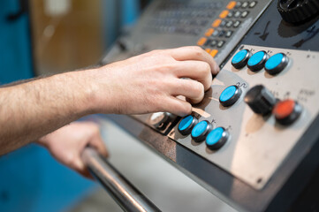 Worker pressing buttons on CNC machine control board in factory. High quality photography.