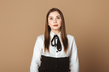 Charming Young Woman Standing Against Beige Studio Background, Gazing Assertively at the Camera. Stylish and Self-assured Female Portraiture in Neutral Setting. Beauty, Confidence, Elegance Concept