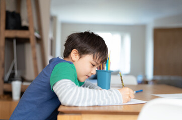 Education, Preschool Kid learning  drawing on white paper,Happy smiling student boy with pencil writing to notebook at home,Child doing homework write and read preparing for exams.