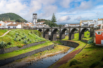Explore the charming architecture and natural beauty of Ribeira Grande, Sao Miguel, through this picturesque view of its iconic arch bridge and serene river setting. - 768119919
