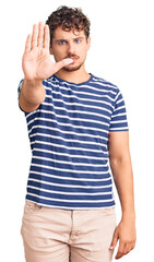 Young handsome man with curly hair wearing casual clothes doing stop sing with palm of the hand. warning expression with negative and serious gesture on the face.