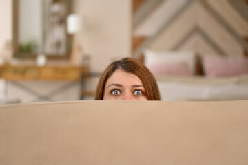 Young woman hides behind a sofa, notices surveillance