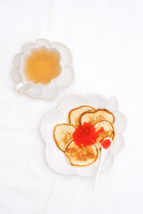  Pancakes with red caviar on white ceramic plate with green tea. White background. Copy space. Top view.