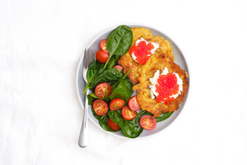 Fried potatoes pancakes with salmon caviar and cream cheese with spinach and tomatoes on white background.