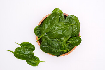 Fresh spinach leaves in wooden bowl on white table. Top view.