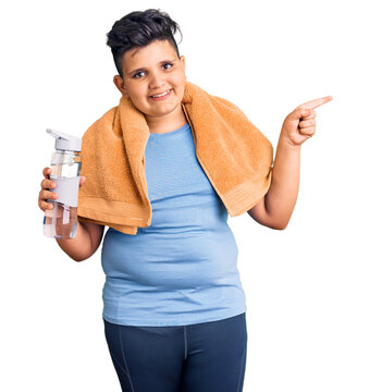 Little boy kid wearing sportswear drinking bottle of water smiling happy pointing with hand and finger to the side