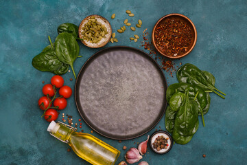 Round dark plate with food ingridients tomatoes, spinach, oil, pumpkin seed, garlic, pepper on dark green background, top view,