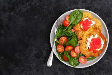 Fried potatoes pancakes with salmon caviar and cream cheese with spinach and tomatoes on black background.