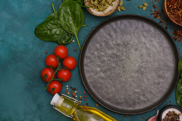 Round dark plate with food ingridients tomatoes, spinach, oil, pumpkin seed, garlic, pepper on green background, top view,