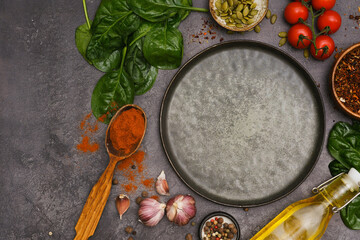 Round dark plate with food ingridients tomatoes, spinach, oil, pumpkin seed, garlic, pepper on dark background, top view,