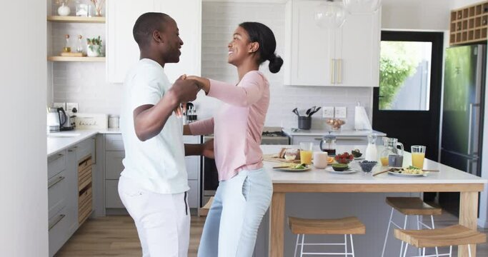 A diverse couple shares a joyful moment dancing together in a bright kitchen