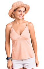 Young blonde woman wearing summer hat winking looking at the camera with sexy expression, cheerful...