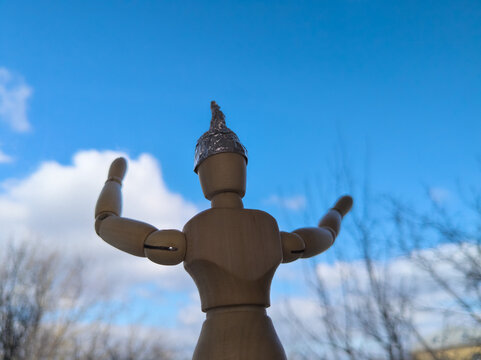A wooden mannequin in a tinfoil hat looks up at the sky.