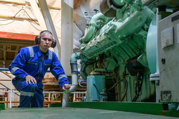 Marine Engineer in blue overall working in Engine room of ship. Work at sea. Motorman.