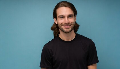 Handsome brunette young man in simple black t-shirt with curly hair smiling to the camera isolated on blue background with copy space, good looking model portrait - obrazy, fototapety, plakaty