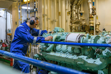 Engineer in blue overall doing service of generator in Engine room of vessel. Work at sea.  Motorman.
