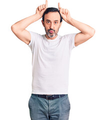 Fototapeta premium Middle age handsome man wearing casual t-shirt doing funny gesture with finger over head as bull horns