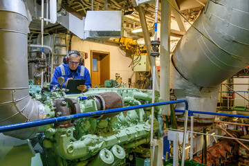 Marine Engineer in blue overall working in Engine room of ship. Work at sea. Motorman.