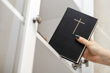 woman takes out a bible from a bookcase