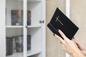 woman reading the bible standing near a bookcase
