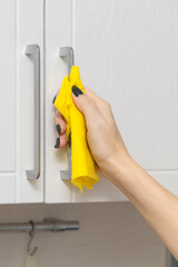 a woman's hand wipes the handle of a kitchen cabinet with a rag