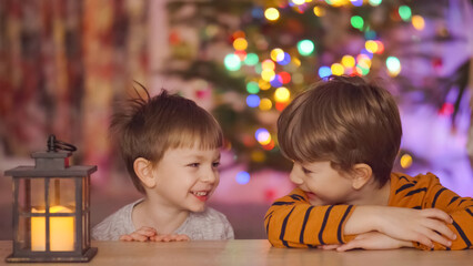 Two little kids near a lantern wait for Santa Claus in front of Christmas tree