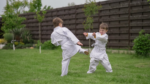Little cheerful funny kids playing karate in white suit in the garden