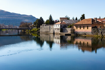 Fototapeta premium Old Town of Trebinje. Calm river reflects the buildings, showcasing minimalism with vivid blue waters and pastel building hues. Bosnia and Herzegovina