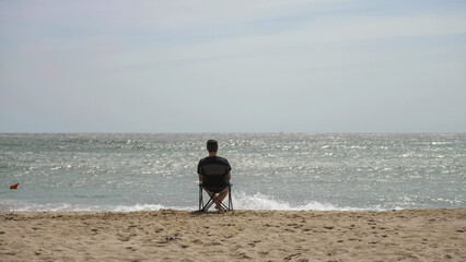 Single young man sitting in fishing chair on the beach