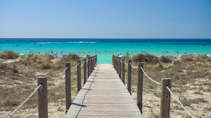 Wooden path over the sandy beach to the turquoise sea of Son Bou in Menorca, Spain