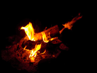 Burning firewood at night. Bonfire in a camping camp in nature in the mountains. Flames and fiery sparks on a dark 