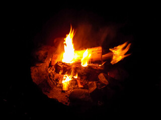 Burning firewood at night. Bonfire in a camping camp in nature in the mountains. Flames and fiery...