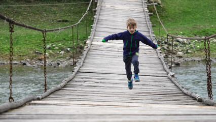 Joyful kid running and jumping on suspended rustic rope bridge