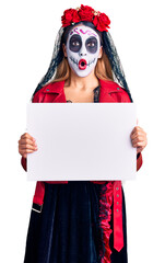 Woman wearing day of the dead costume holding blank empty banner scared and amazed with open mouth for surprise, disbelief face