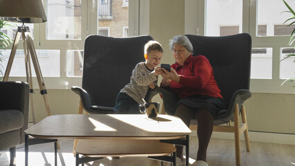 Little kid and his grandmother reading a tale on mobile phone