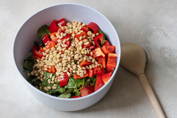 Green salad with tomatoes, red pepper, cilantro greenery and pine nuts in bowl