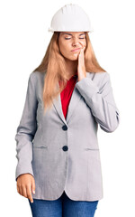 Beautiful young woman wearing architect hardhat touching mouth with hand with painful expression because of toothache or dental illness on teeth. dentist