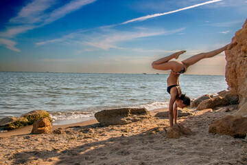 Fototapeta na wymiar Beautiful girl - yoga stands on her hands against the background of the sea 