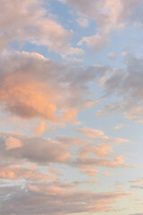 Pastel sunset sky with soft pink and blue hues among fluffy clouds, offering a gradient of warm to...