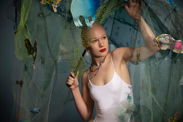 A bald woman poses elegantly with vibrant floating sea life decorations and a white dress, showcasing confidence