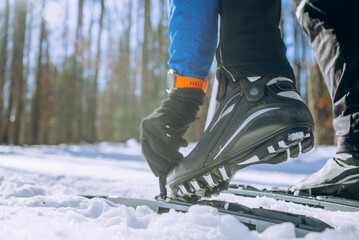 Close-up of Cross-Country Skier Fastening Ski Boots in Snow. A male athlete's hand in a glove and a sports watch fastens a ski mount, doing outdoor sports.