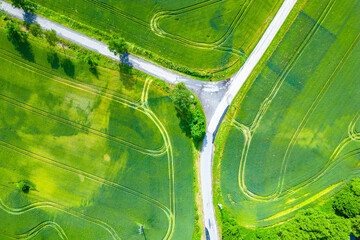 Aerial shot captures the serene beauty of intersecting roads amidst lush green fields. The image...