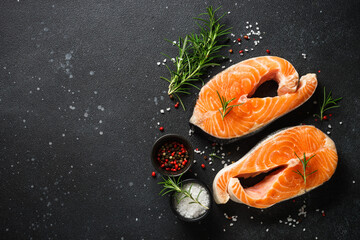 Raw salmon steaks on cutting board at black background. Top view with ingredients for cooking.
