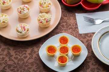 Red caviar in tartlets on a plate and salad on a brown tablecloth