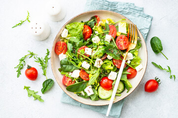 Green salad with spinach, arugula and tomatoes with olive oil. Top view on white.