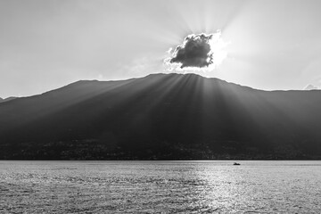 Fototapeta premium A tranquil scene capturing the serene beauty of a mountain lake at sunset. Sun rays pierce through a cloud, casting illuminating beams and sparkling reflections on the water surface. A lone boat