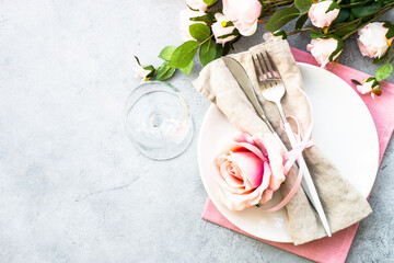 White plate, cutlery and wine glass with pink flowers. Spring table settong. Flat lay with copy space.