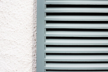 Close-up of painted French style shutters in grey green against a painted textured white wall 