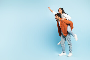 indian man giving piggyback ride to wife against blue backdrop